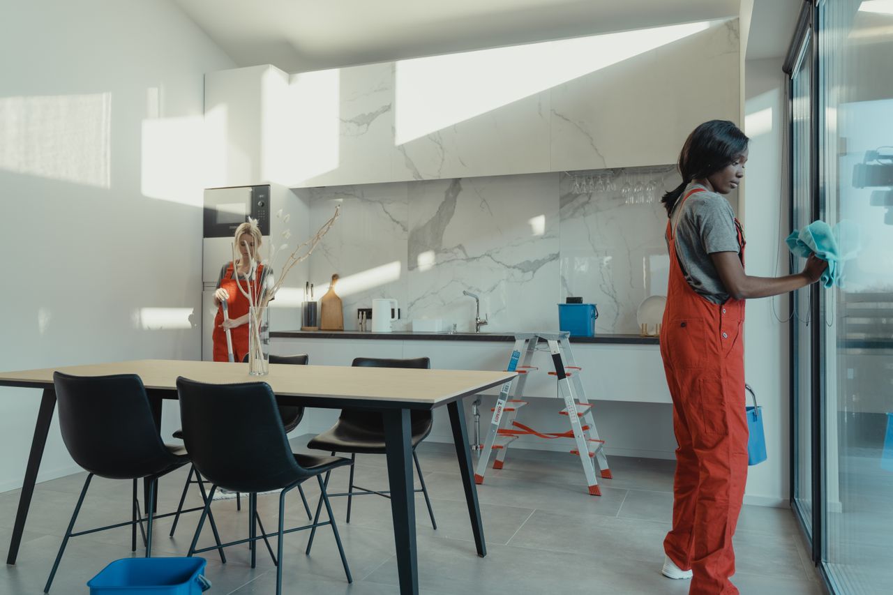 gallery-03 Two women in work clothes cleaning a kitchen with glass doors.