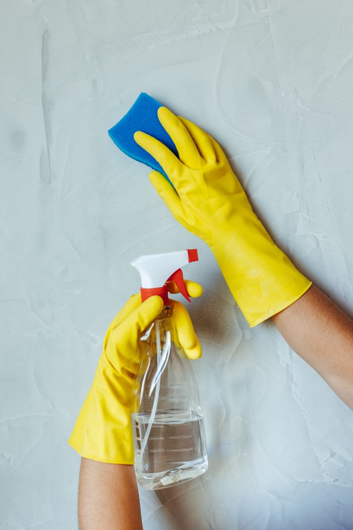 services-img Hands in yellow gloves cleaning wall with sponge and spray bottle.
